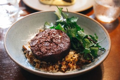Medalhão de carne sobre grãos, com folhas verdes ao lado, num prato fundo.