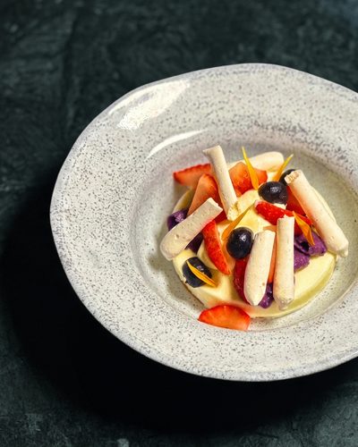Sobremesa com frutas frescas e bastões claros sobre creme, num prato texturizado.